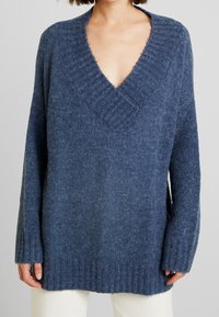 Pullover overdimensionato blu navy realizzato in morbida lana, caratterizzato da un profondo scollo a V, polsini e orlo ribattuti, con un aspetto testurizzato.