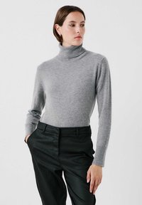 Grå poloavskuren tröja i mjukt stickat material, med figurnära långa ärmar och en slät yta. Matchad med skräddarsydda svarta byxor.