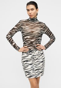 Διαφανές μακρυμάνικο τοπ σε μαύρο και μπεζ με ζιβάγκο, σε συνδυασμό με εφαρμοστή μπεζ φούστα με μαύρο σχέδιο ζέβρας.