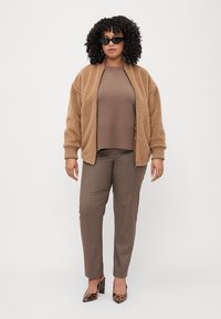 Veste en polaire marron, pull marron côtelé et pantalon marron ajusté. Les accessoires comprennent des lunettes de soleil noires et des talons imprimés léopard.