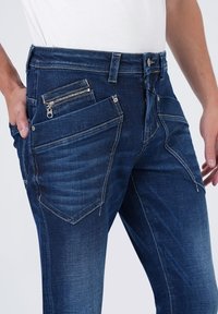 Denim jeans in een donkerblauwe was, met meerdere zakken, waaronder een met rits, en contrasterende stiksels.