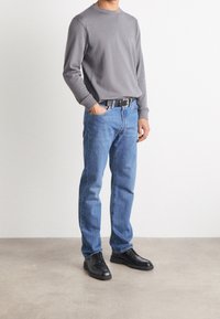 Maglietta grigia a manica lunga, jeans blu, scarpe nere. La maglietta ha un collo tondo; i jeans hanno un taglio classico e sono leggermente consumati.