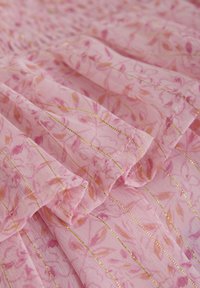 Ljusrosa tyg med blommönster och gyllene vertikala ränder. Har mjuka, texturerade veck och en delikat detaljering.