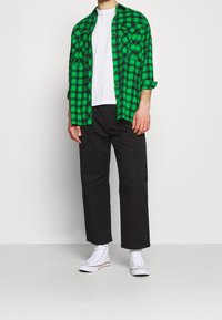 Vihreä ja musta ruudullinen flanellipaita valkoisen T-paidan päällä, yhdistettynä mustiin housuihin ja valkoisiin korkeavartisiin tennareihin.