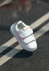 White athletic shoe with pink accents and gray textured details, featuring two adjustable velcro straps and perforations for breathability.