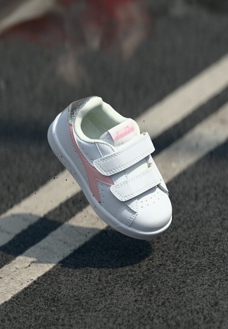 White athletic shoe with pink accents and gray textured details, featuring two adjustable velcro straps and perforations for breathability.