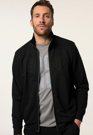 Black zip-up jacket with a stand collar and large textured "IRON" lettering. Worn over a gray t-shirt featuring bold letters.