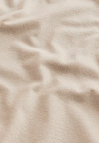 Beige szövet sima textúrával és finom fénylő felülettel, amely lágy gyűrődéseket és redőket mutat, jelezve a rugalmasságot és a puhaságot.