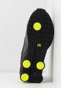 Černá podrážka sportovní obuvi, s kruhovými žlutými akcenty a drsnou gumou pro lepší přilnavost. Design zahrnuje vzorované drážky pro trakci.