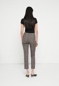 Pantaloni mulați cu imprimeu leopard, confecționați dintr-un material ușor, cu un luciu subtil, asortați cu sandale negre cu vârf decupat și un top negru mulat.