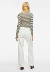 Camiseta de manga larga a rayas en colores negro y crema, combinada con pantalones anchos blancos. Tejido suave con una silueta ajustada. Zapatos de tacón marrones.