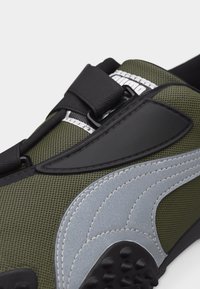 Πράσινο και γκρι αθλητικό παπούτσι Puma με υφασμένο δίχτυ, μαύρο ρυθμιζόμενο λουράκι κλεισίματος και εμφανές λογότυπο της μάρκας στη γλώσσα.