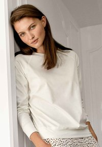 Cream-colored sweatshirt with a round neckline and raglan sleeves, paired with patterned bottoms. Smooth texture, fitted cuffs, and hem.