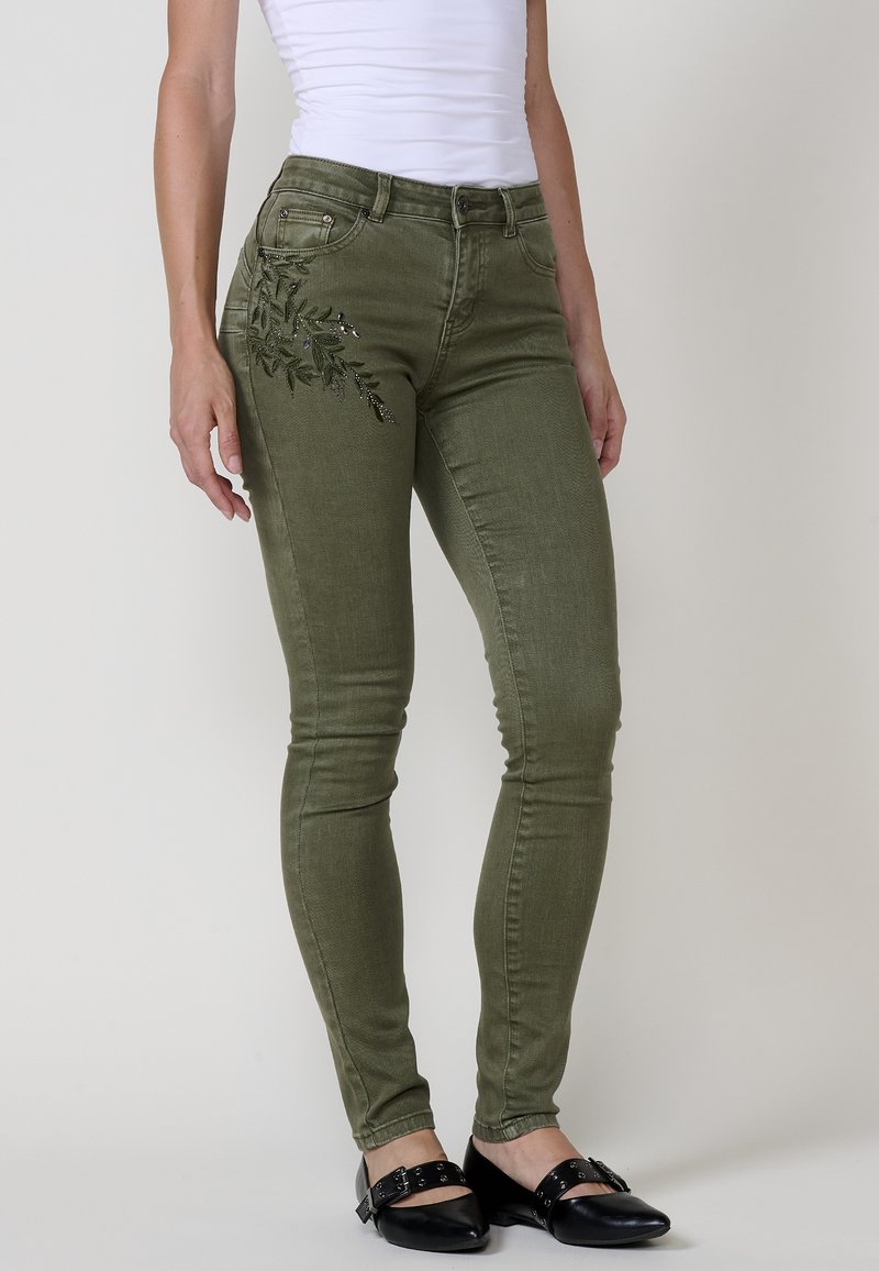 Olivově zelené skinny džíny s boční výšivkou listů. Mají středně vysoký pas a klasický pětikapsový design. Hladká textura.
