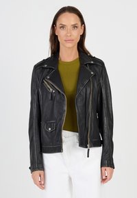 Schwarze Leder-Motorradjacke mit asymmetrischem Reißverschluss, silberner Hardware und Seitentaschen. Trägt man über einem grünen gerippten Oberteil.