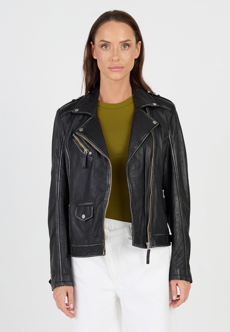 Schwarze Leder-Motorradjacke mit asymmetrischem Reißverschluss, silberner Hardware und Seitentaschen. Trägt man über einem grünen gerippten Oberteil.