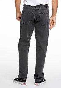 Jeans de mezclilla negra con corte recto, que presentan bolsillos traseros, sutiles efectos de desgaste y zapatos negros usados.