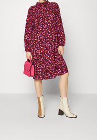 Czarna sukienka z długim rękawem i różowo-czerwonym kwiatowym wzorem, z falbaną na dole. Połączona z beżowymi i brązowymi botkami na słupku.