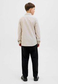 Camicia button-up beige chiaro con una cucitura sulla schiena e maniche lunghe, abbinata a pantaloni e scarpe neri. Design semplice e sartoriale.