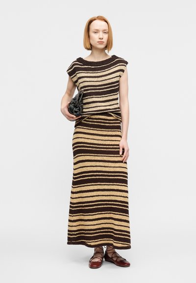 Πλεκτό σετ δύο τεμαχίων με οριζόντιες καφέ και μπεζ ρίγες· αμάνικο τοπ με φαρδιά λαιμόκοψη, μακριά φούστα και καφέ αξεσουάρ.