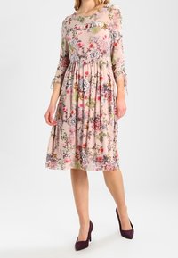 Vestido estampado floral con mangas tres cuartos, en tela de color rosa claro; cintura ceñida, a la altura de la rodilla, con vibrantes flores multicolores.