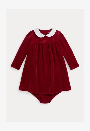 Robe en velours rouge à manches longues, col Peter Pan blanc, corsage froncé et bas bouffant attaché. Détail de logo discret sur la poitrine.