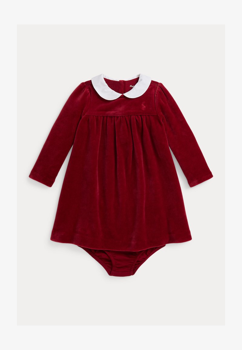 Vestido de veludo vermelho com mangas longas, colarinho Peter Pan branco, corpete drapeado e parte inferior em calções acoplados. Pequeno detalhe de logotipo no peito.