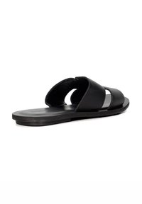 Black leather slide sandal featuring two wide straps with cutout design, flat sole, and textured upper, providing a minimalist aesthetic.