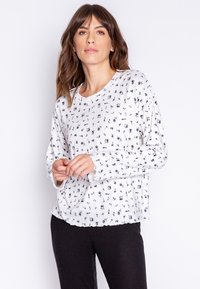 Vit långärmad topp med svart blommönster, rund halsringning och lätt texturerad tyg. Har gatherdetaljer vid nederkanten och vågiga manschetter.