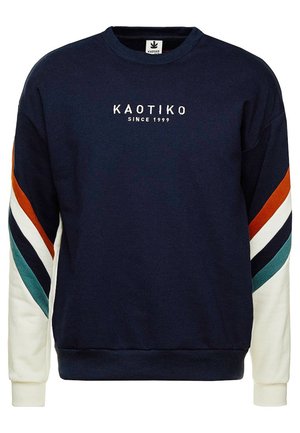 Mørk blå genser laget av bomull, med flerfargede stripede detaljer og rund hals. Logoen "KAOTIKO" og "SINCE 1999" brodert foran.