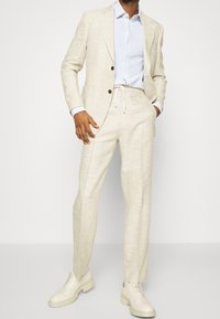 Beige linnen blazer met twee knopen, lichtblauw polka-dot shirt, trekkoordbroek en off-white veterschoenen. Glad textuur in het geheel.