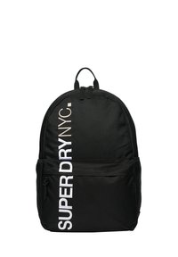 Czarny plecak z materiału, wyróżniający się okrągłym kształtem, wyraźnym białym napisem "SUPERDRY NYC" oraz podwójnym zapięciem na zamek i uchwytem u góry.