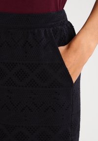 Gonna nera con texture caratterizzata da un motivo e tasca laterale, realizzata in tessuto morbido con una vita comoda.