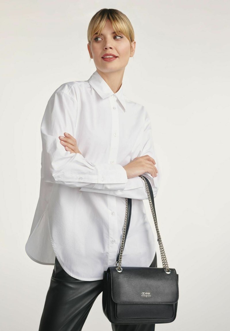 Czarna skórzana torebka z fakturowanym wykończeniem i srebrnym łańcuszkiem. Torebka ma zapięcie na klapę oraz wypolerowany akcent z logo.