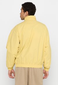 Lys gul, letvægtsjakke med høj krave, elastisk talje og let oversized design. Velegnet til afslappet brug.