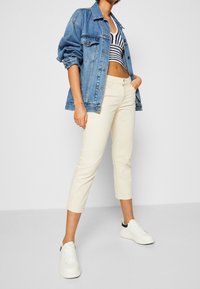 Spijkerjack in lichtblauw, cropped witte broek en witte sneakers met zwarte accenten. De outfit heeft een gestreept zwart-wit topje.