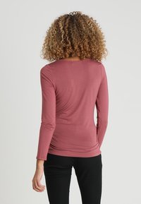 Långärmad topp i dämpad rosafärg, med rundad halsringning, figurnära design och texturerad fåll. Styla med mörka byxor.