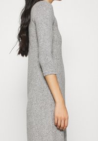 Abito in maglia grigio chiaro, con maniche a tre quarti, vestibilità slim, texture morbida e scollo rotondo. La vista laterale enfatizza la silhouette allungata.