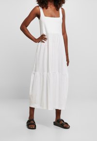 Biała, bezrękawnikowa sukienka maxi o kwadratowym dekolcie i warstwowym dole. Wykonana z lekkiego materiału, charakteryzuje się luźnym krojem i casualowym stylem.