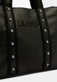 Sac fourre-tout noir texturé avec des clous en argent le long des bords, orné d'un contraste en fourrure noire douce et d'un détail de logo en relief.