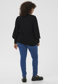 Black pullover sweater with puff sleeves, paired with blue fitted jeans and black platform shoes, viewed from the back.