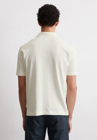 Light beige polo shirt with short sleeves, made of textured fabric. Features a classic collar and side slits at the hem for comfort.