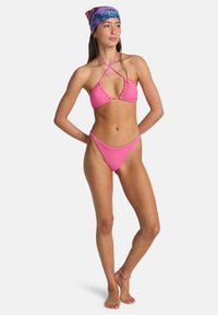 Bikini rosa a coste con top a triangolo e slip a vita alta. La modella indossa un foulard multicolore. Design minimalista che mette in risalto le caratteristiche.