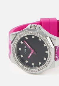 Oktagonal silverur med svart urtavla, rosa detaljer, kristallbesatt boett och ett klart rosa silikonarmband med ett strukturerat mönster.
