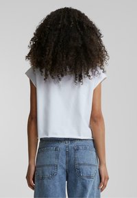T-shirt blanc court à manches courtes, fabriqué en coton doux, associé à un jean bleu délavé taille haute avec de grandes poches arrière.