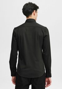 Black long-sleeve shirt with a smooth texture, tailored fit, button cuffs, and a classic collar, viewed from the back.