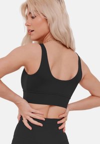 Black sports bra with a wide scoop neckline and thick straps, featuring a fitted design and smooth texture, ending just above the waist.