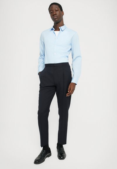 Lys blå button-up skjorte med spredt krage, parret med mørk marineblå skræddersyede bukser og sorte loafers. Glat stof og tætsiddende design.