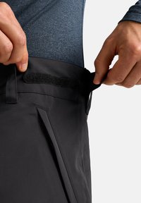 Zwarte outdoor broek met een met klittenband verstelbare tailleband. Soepele textuur, rechte pijpdesign en zichtbare zijzakken.
