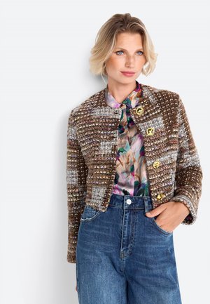 Brown and gray textured jacket with gold buttons, worn over a floral blouse, paired with high-waisted blue denim jeans.